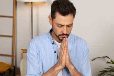 Man with clasped hands praying in room at home