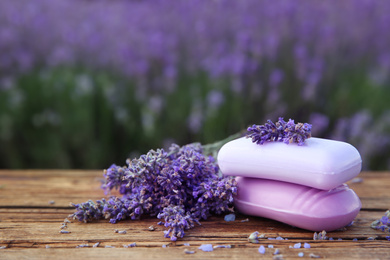 Photo of Fresh lavender flowers and soap bars on wooden table outdoors, closeup