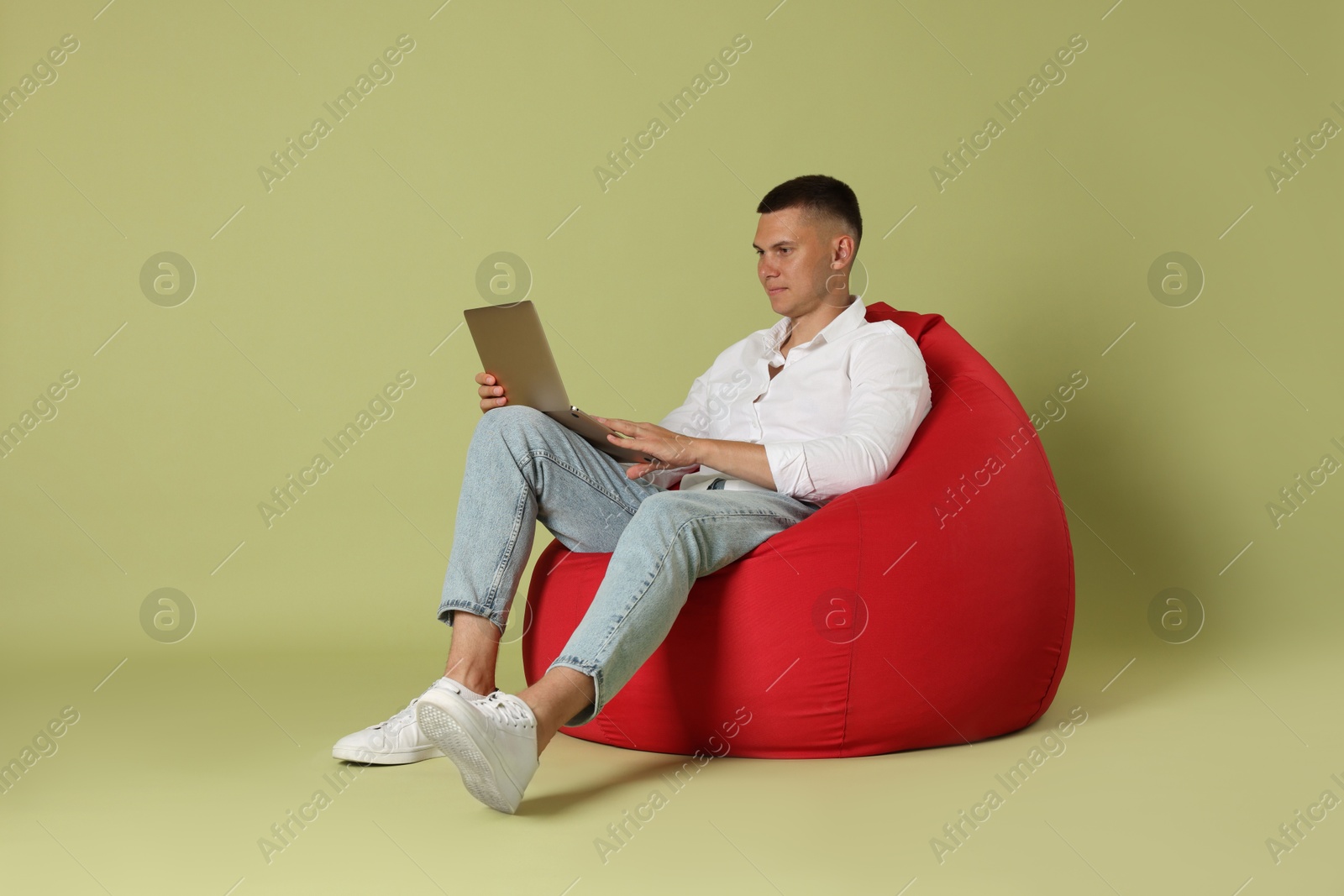 Photo of Handsome man with laptop on red bean bag chair against green background