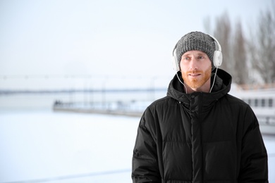 Photo of Young man listening to music with headphones outdoors. Space for text