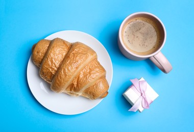 Photo of Romantic breakfast with cup of coffee, croissant and gift box on turquoise background, flat lay. Valentine's day celebration