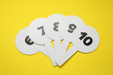 Auction paddles with numbers on yellow background, flat lay