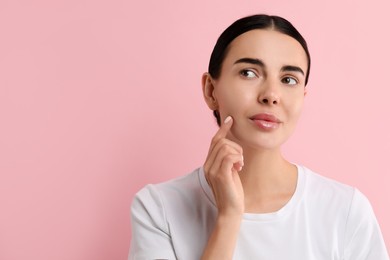 Woman with dry skin checking her face on pink background, space for text