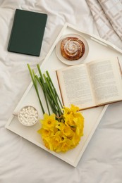 Bouquet of beautiful daffodils, bun and coffee on bed, top view