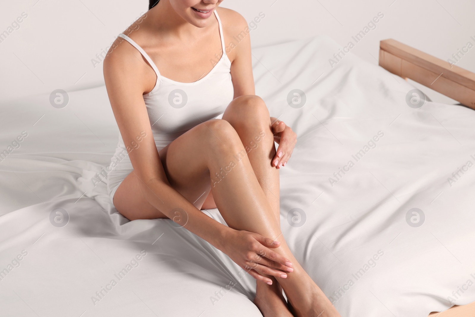 Photo of Woman with beautiful smooth legs sitting on bed at home, closeup