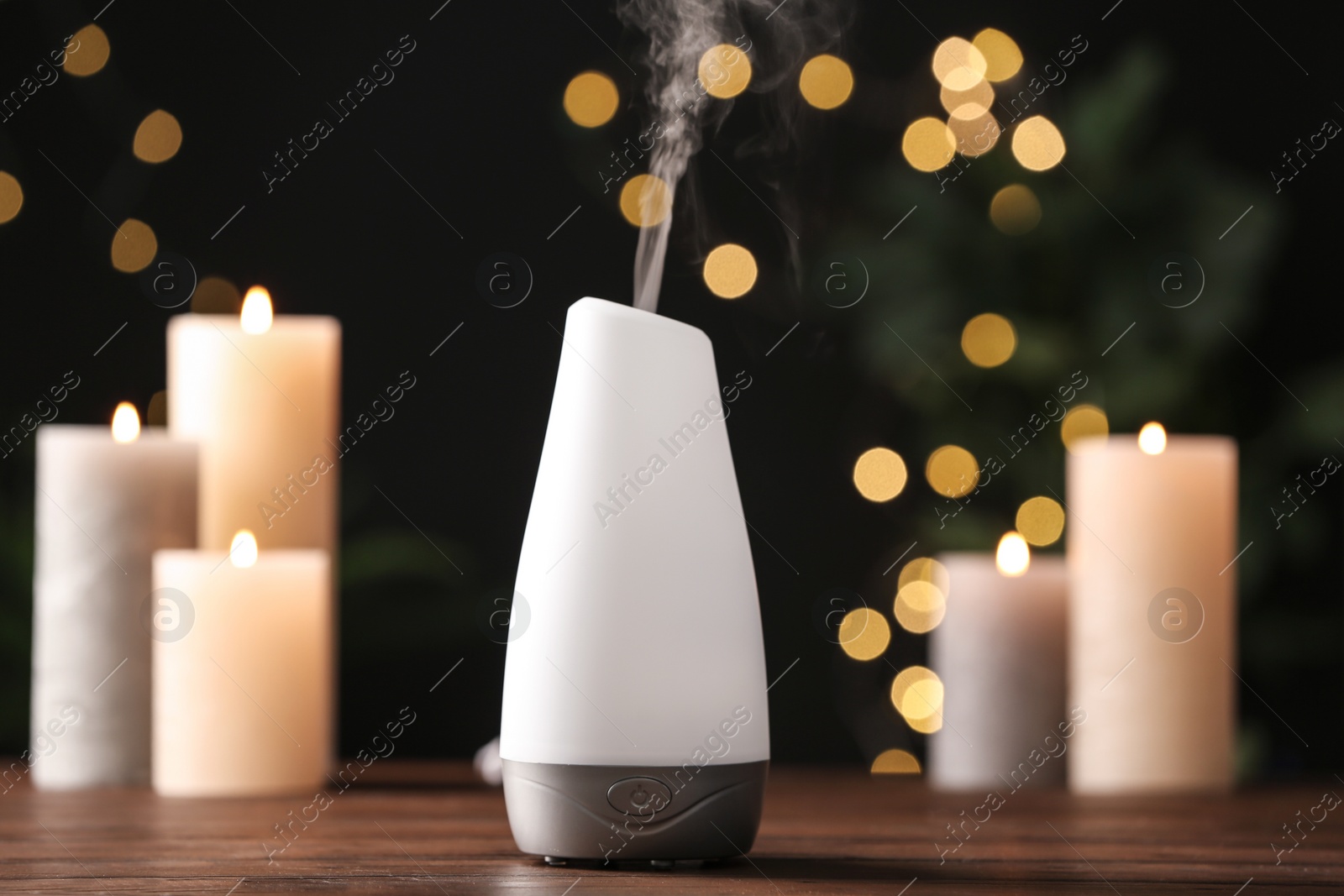 Photo of Modern aroma humidifier with candles on wooden table against blurred lights, space for text