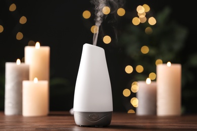Photo of Modern aroma humidifier with candles on wooden table against blurred lights, space for text