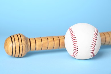 Photo of Wooden baseball bat and ball on light blue background, closeup. Sports equipment