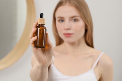 Woman with bottle of essential oil indoors, selective focus. Space for text