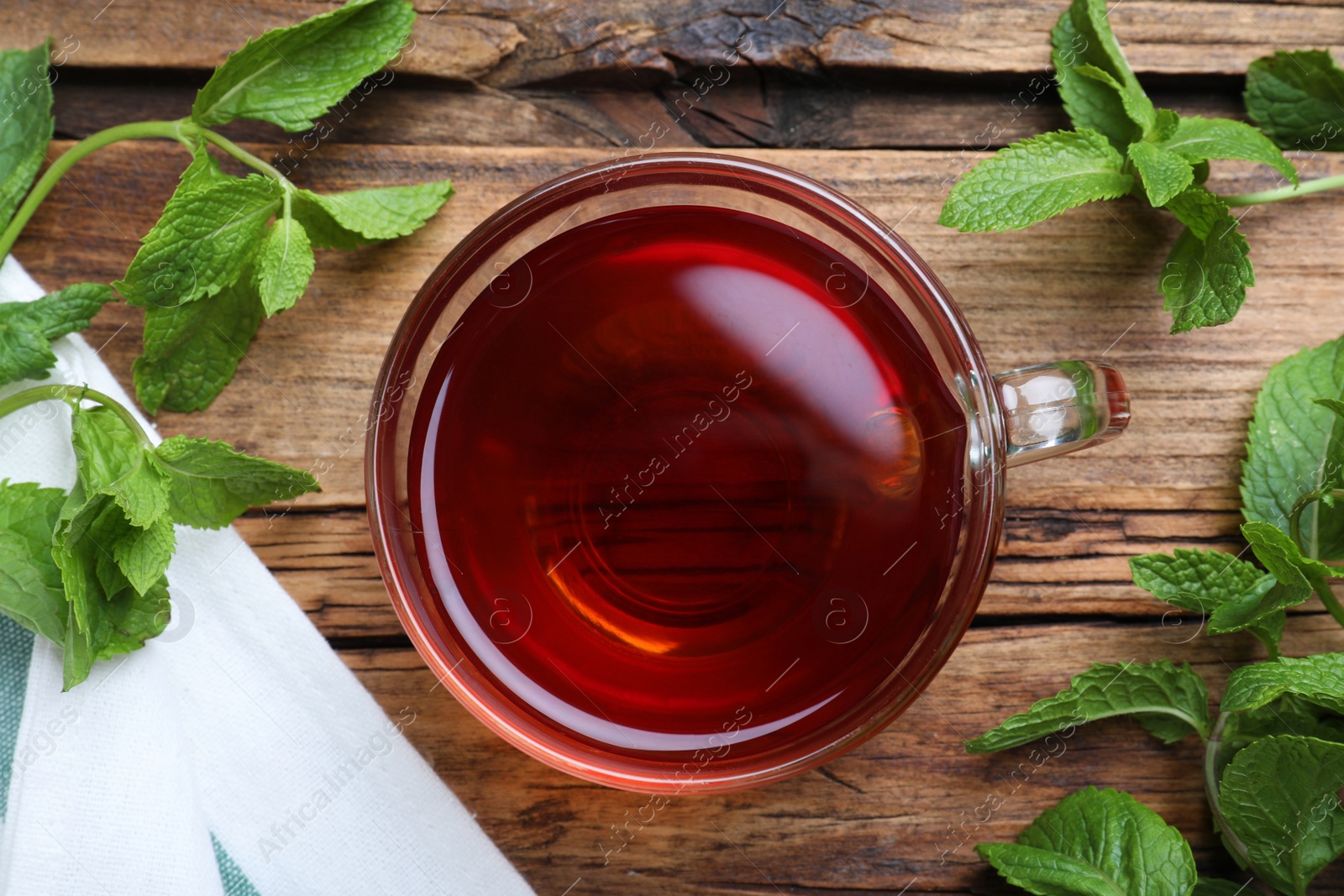 Photo of Cup with hot aromatic mint tea and fresh leaves on wooden table, flat lay