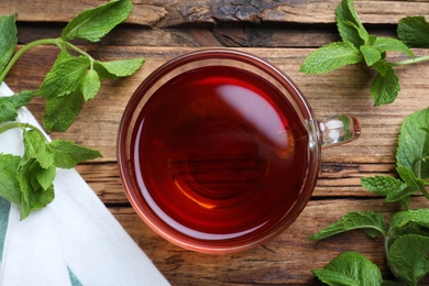 Photo of Cup with hot aromatic mint tea and fresh leaves on wooden table, flat lay