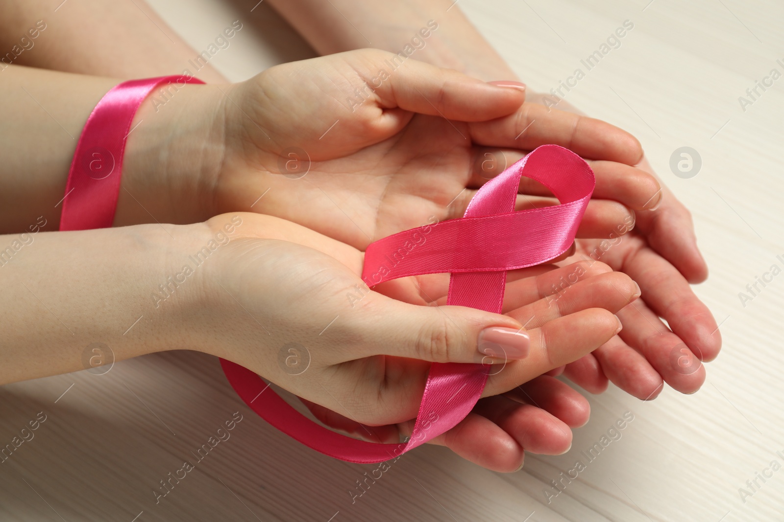 Photo of Women holding pink ribbon at white wooden table, closeup. Breast cancer awareness