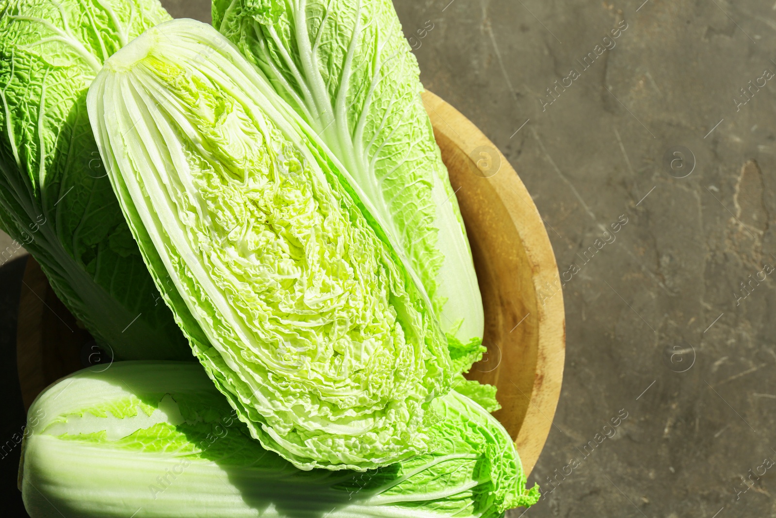 Photo of Fresh ripe Chinese cabbages in bowl on gray textured table, top view