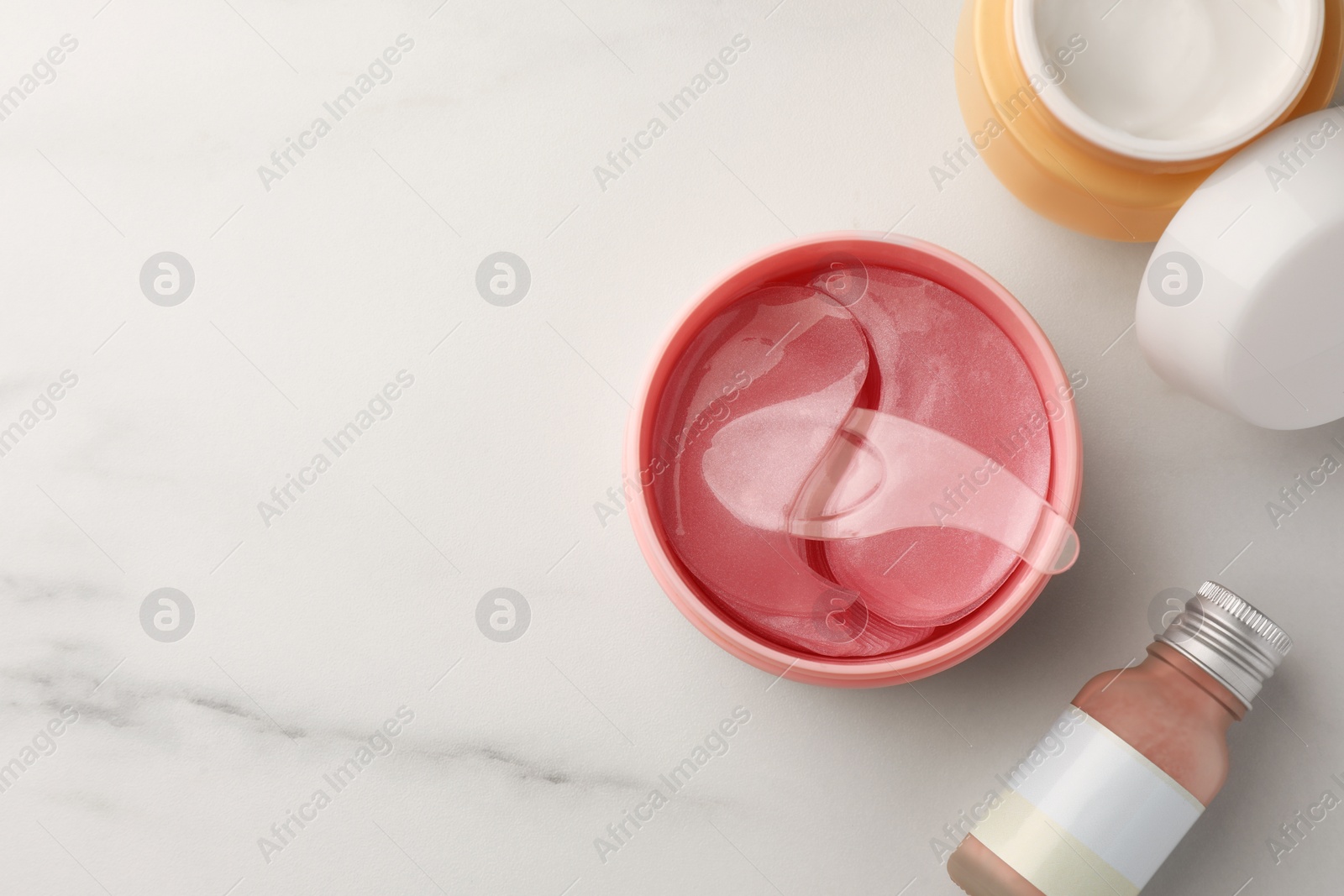 Photo of Jar of under eye patches with spoon and cosmetic products on white marble table, flat lay. Space for text