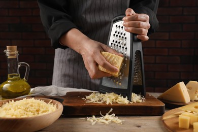 Photo of Woman grating cheese at wooden table, closeup