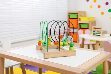 Photo of Toy bead maze on wooden table in playroom. Kindergarten interior design