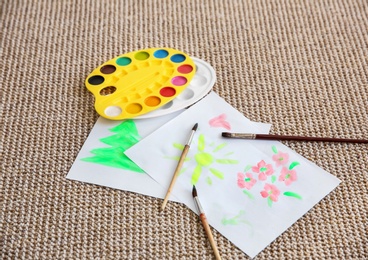 Photo of Paintings with palette and brushes on carpet