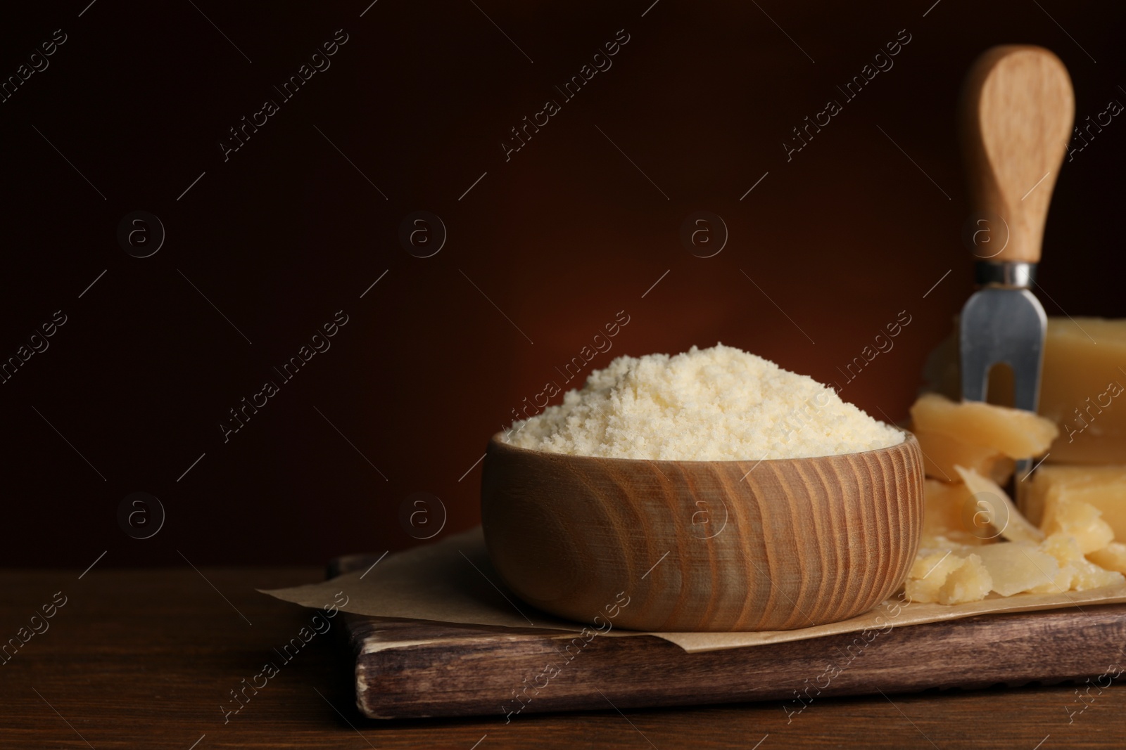 Photo of Delicious grated parmesan cheese in bowl on wooden table, space for text