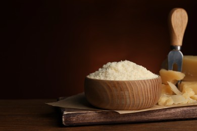 Photo of Delicious grated parmesan cheese in bowl on wooden table, space for text