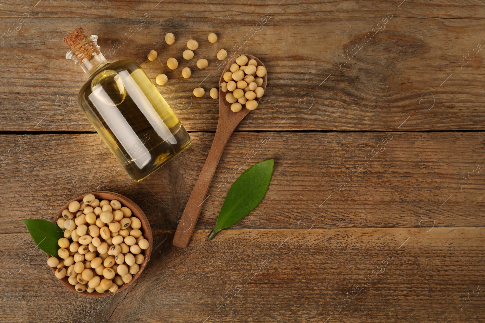 Photo of Glass bottle of oil, leaves and soybeans on wooden table, flat lay. Space for text