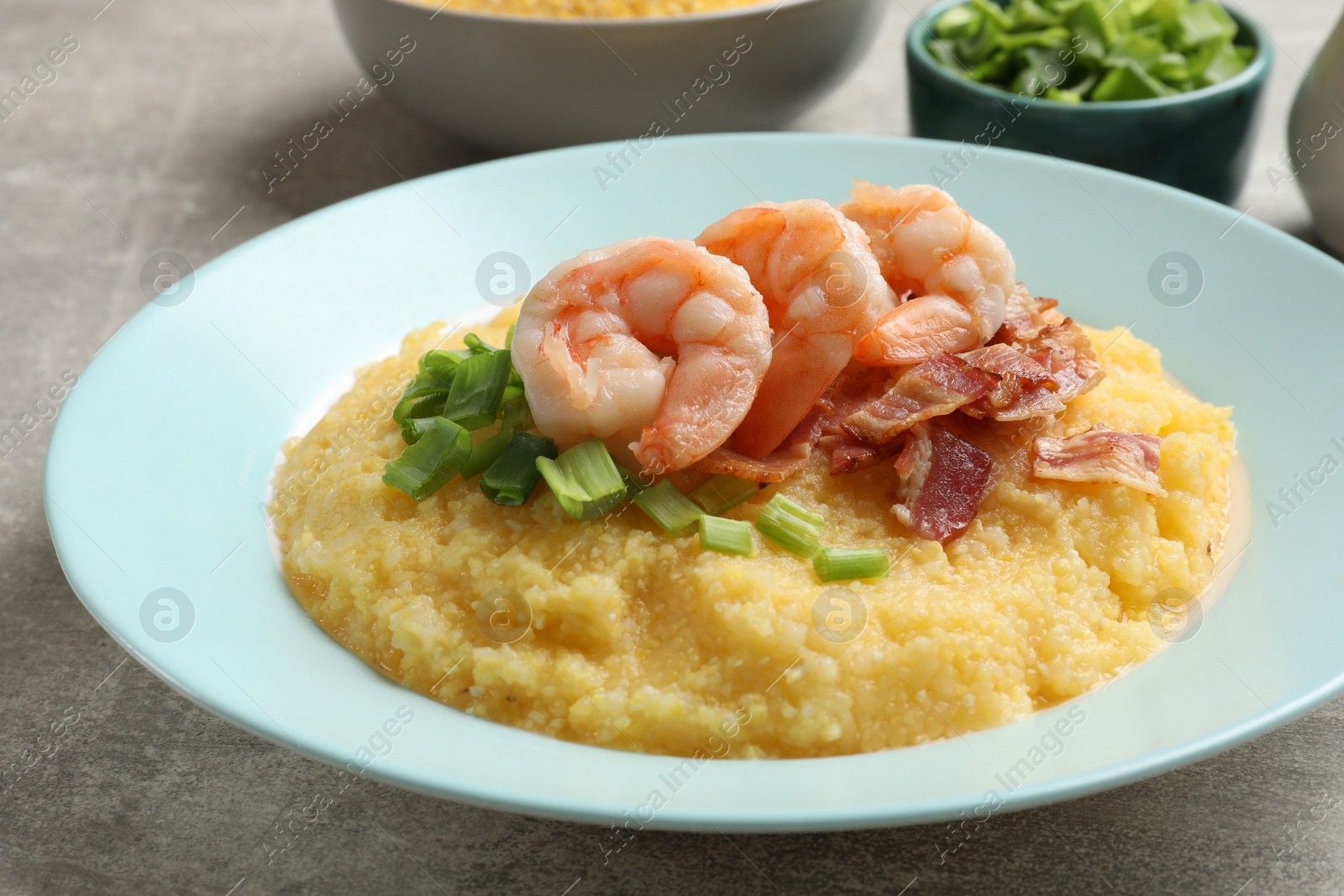 Photo of Plate with fresh tasty shrimps, bacon, grits and green onion on grey table, closeup