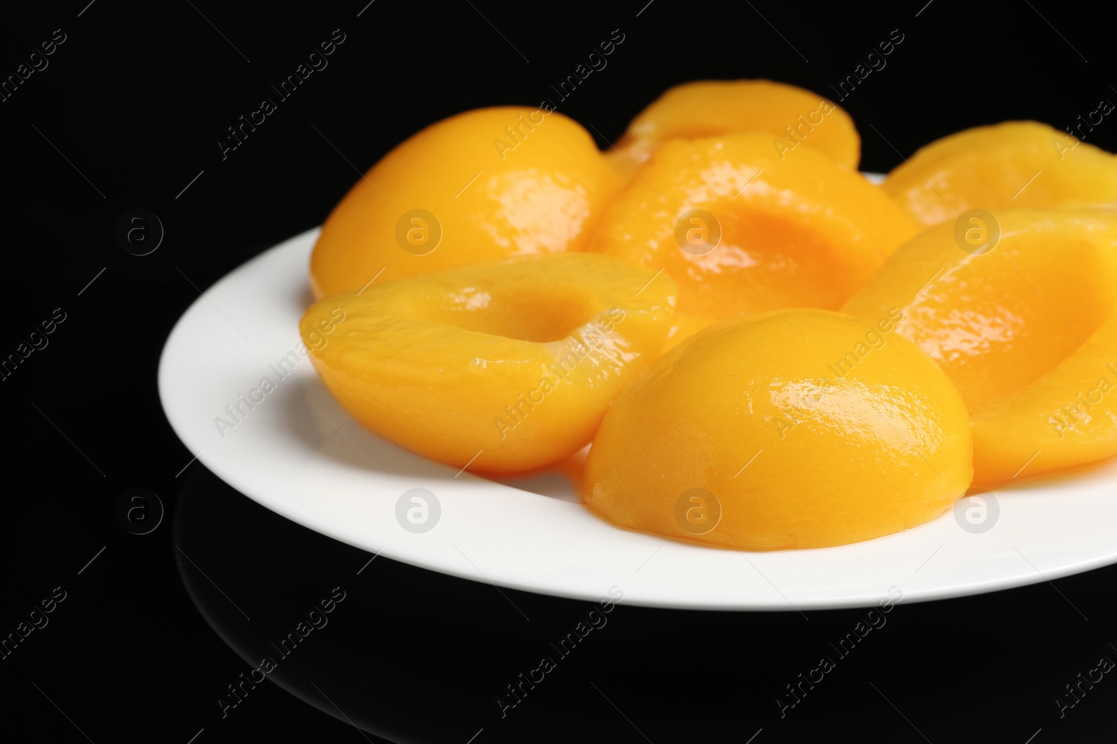 Photo of Plate with canned peach halves on black background, closeup