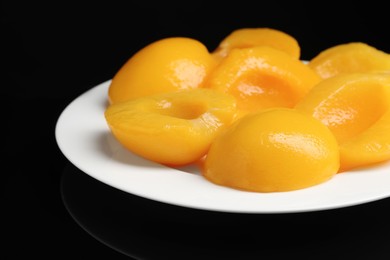 Plate with canned peach halves on black background, closeup