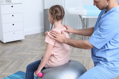 Orthopedist helping child to do exercise with dumbbell in clinic. Scoliosis treatment