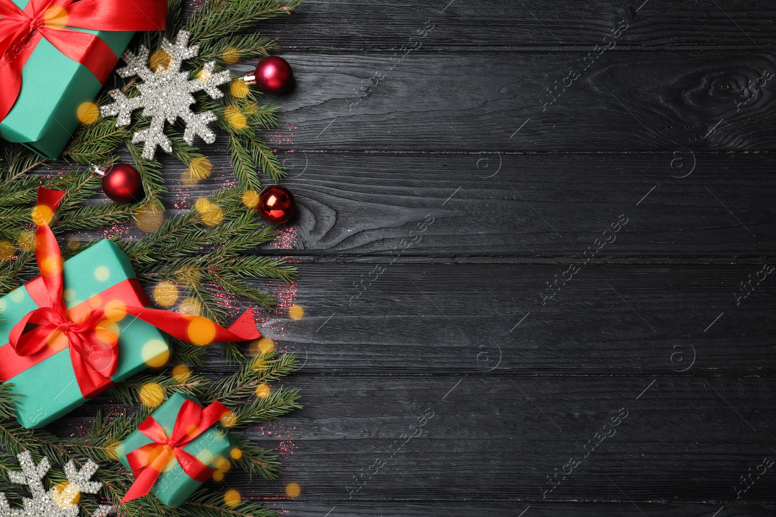 Photo of Christmas greeting card with space for text. Flat lay composition of fir tree branches and festive decor on black wooden background