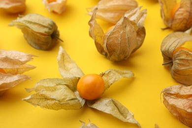 Ripe physalis fruits with calyxes on yellow background, closeup