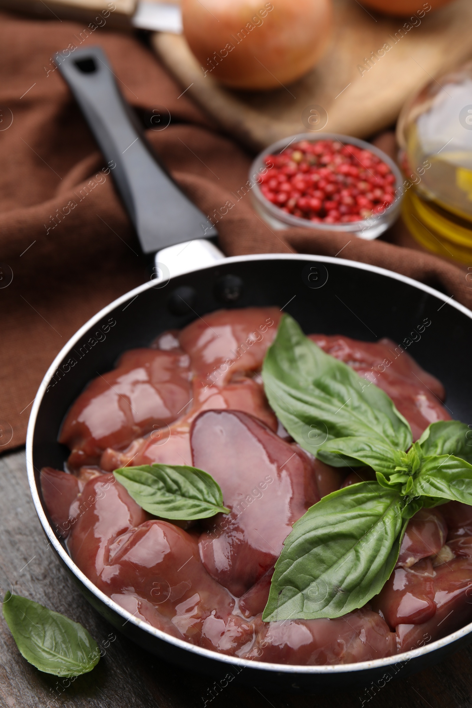 Photo of Raw chicken liver with basil in frying pan on wooden table, closeup