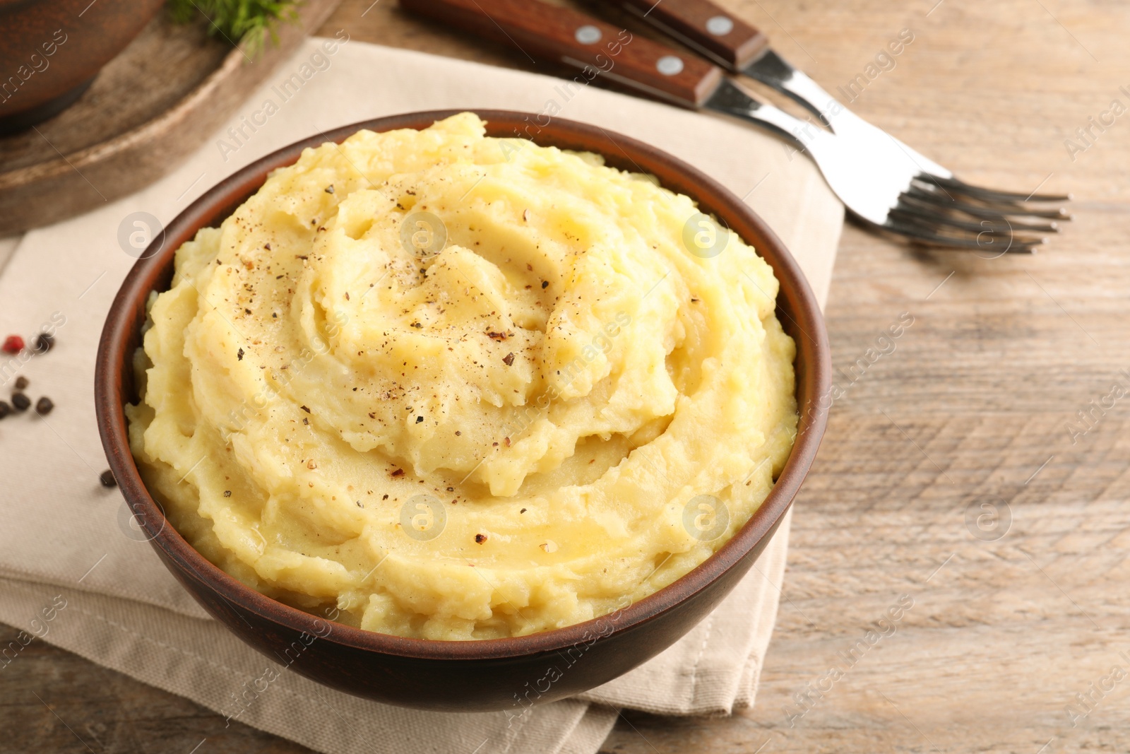 Photo of Bowl of tasty mashed potatoes with black pepper served on wooden table