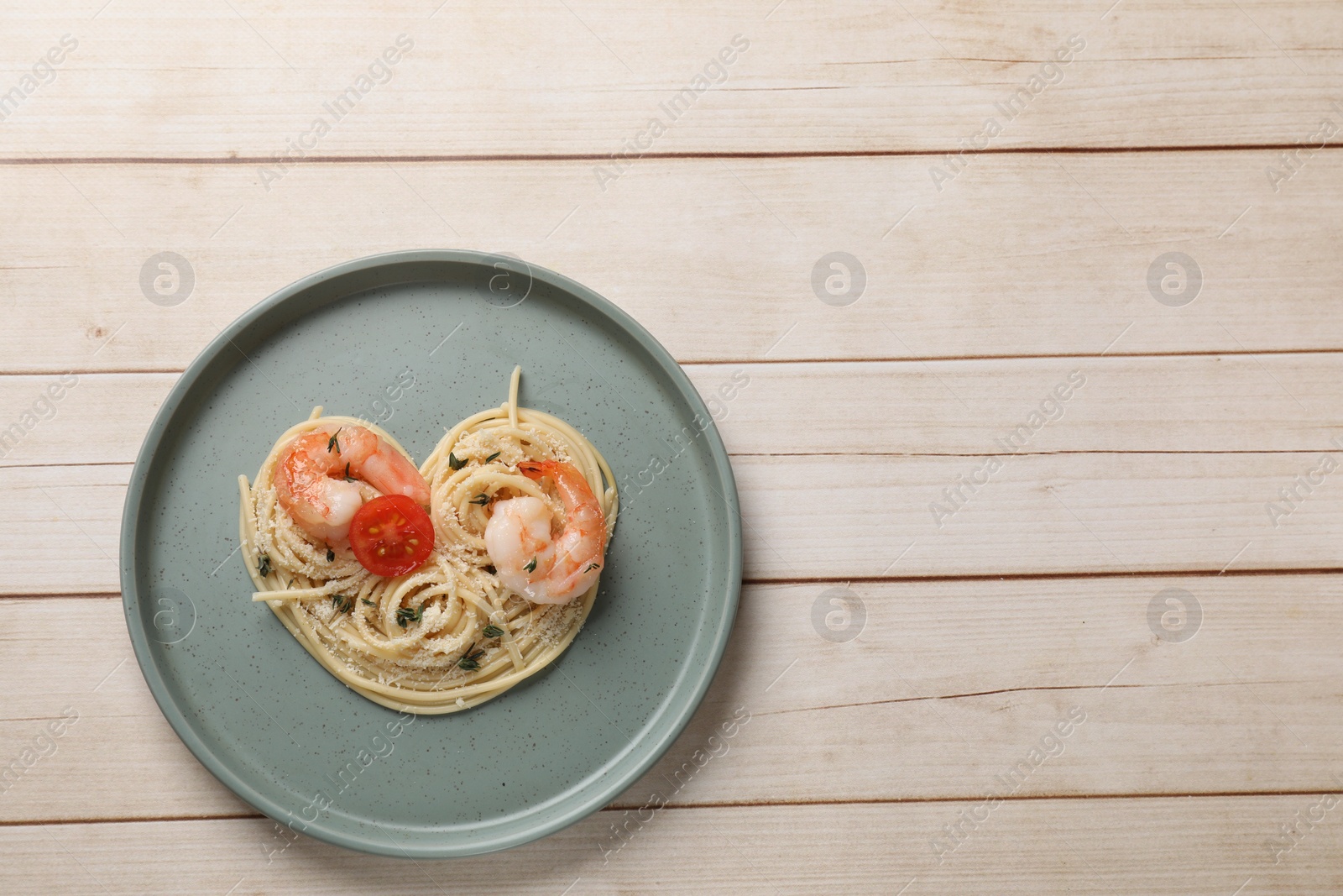 Photo of Heart made of tasty spaghetti, tomato, shrimps and cheese on light wooden table, top view. Space for text