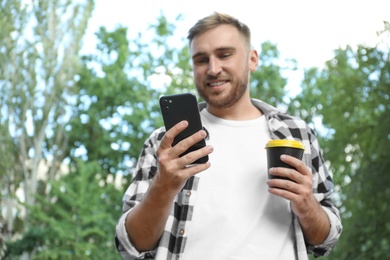 Photo of Young man with smartphone and cup of coffee in park