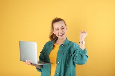 Portrait of beautiful young woman with laptop on yellow background