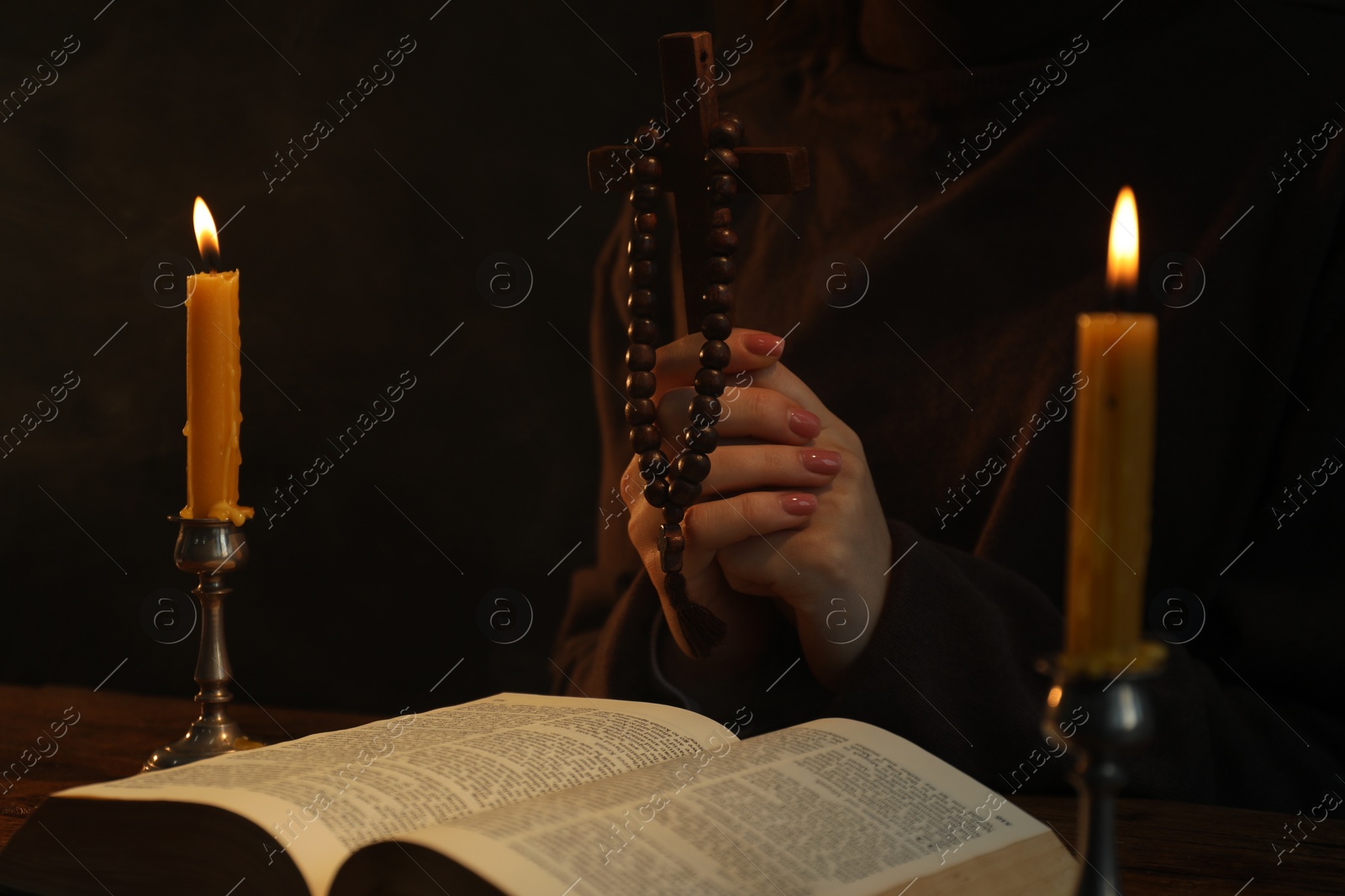 Photo of Woman praying at table with burning candles and Bible, closeup