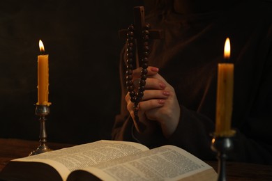 Woman praying at table with burning candles and Bible, closeup