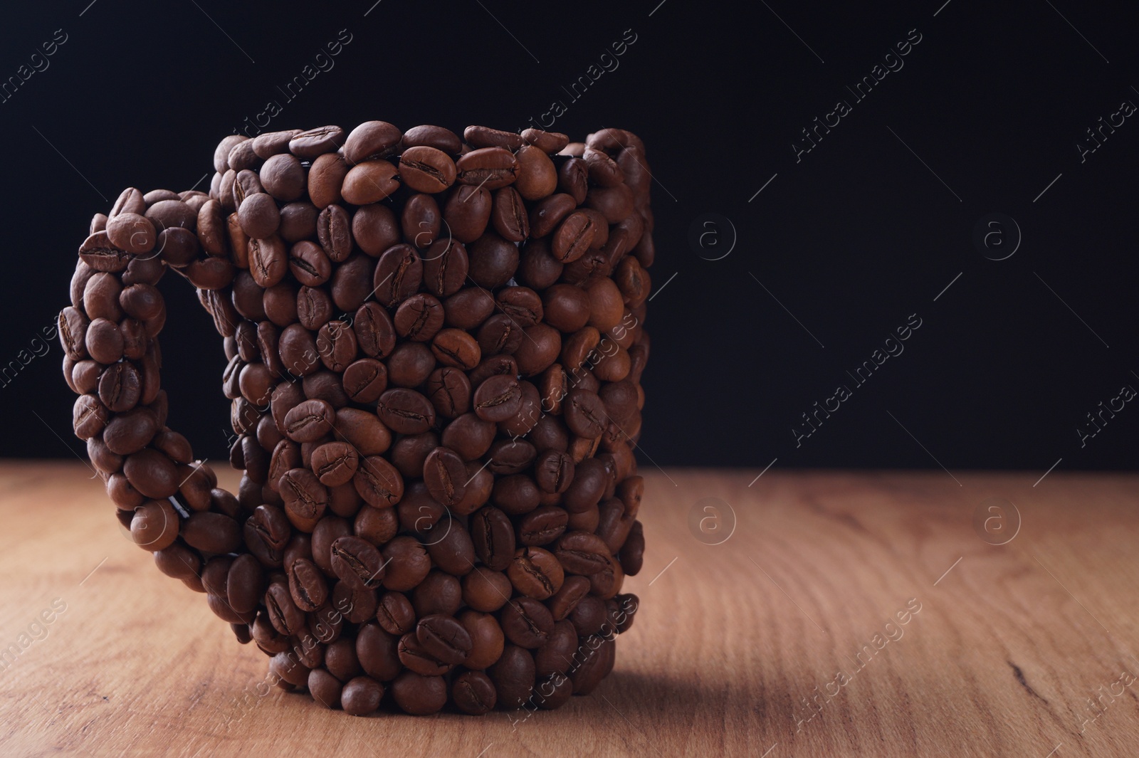 Photo of Cup made of coffee beans on wooden table against black background. Space for text