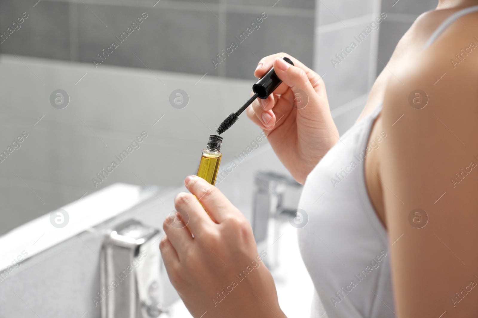 Photo of Young woman with eyelash oil in bathroom, closeup