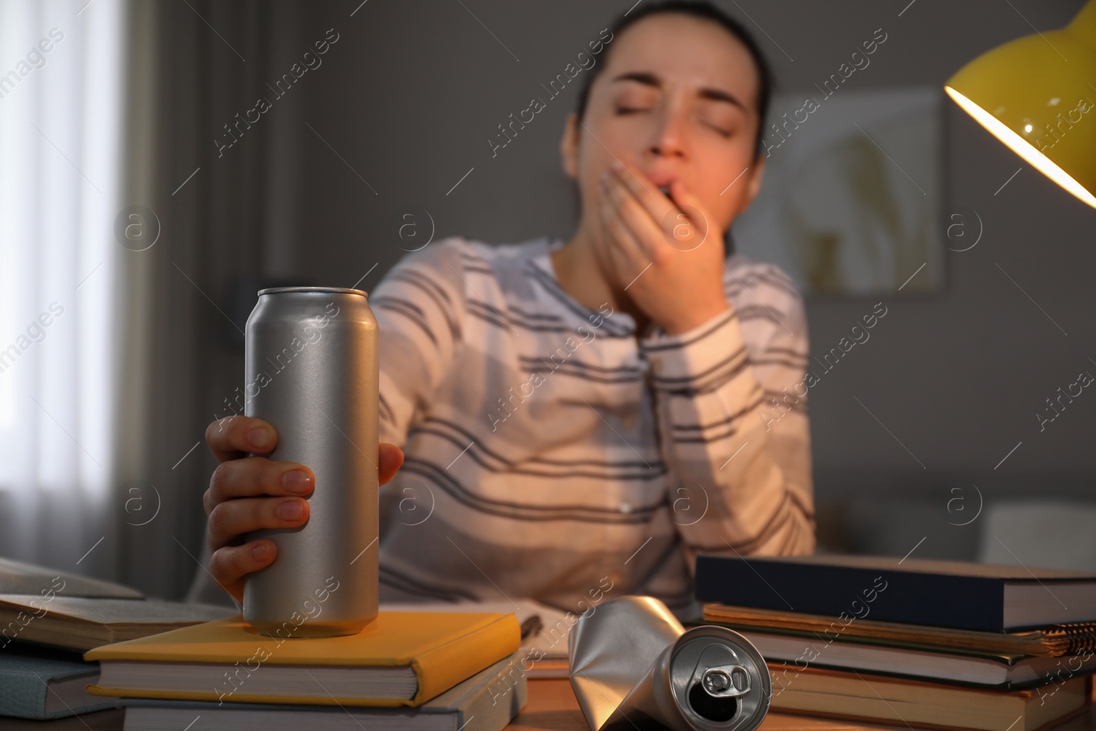 Photo of Tired young woman with energy drink studying at home, focus on hand