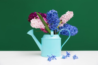 Photo of Beautiful hyacinths in watering can on table against color background. Spring flowers