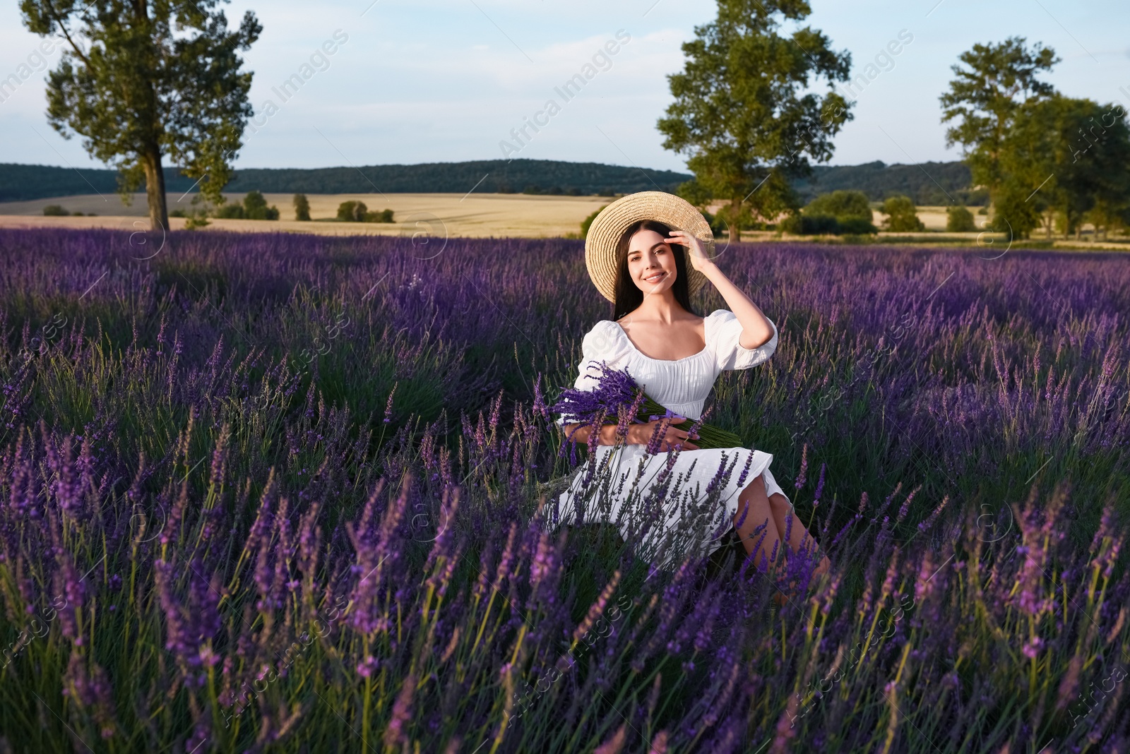 Photo of Beautiful young woman sitting in lavender field at sunset