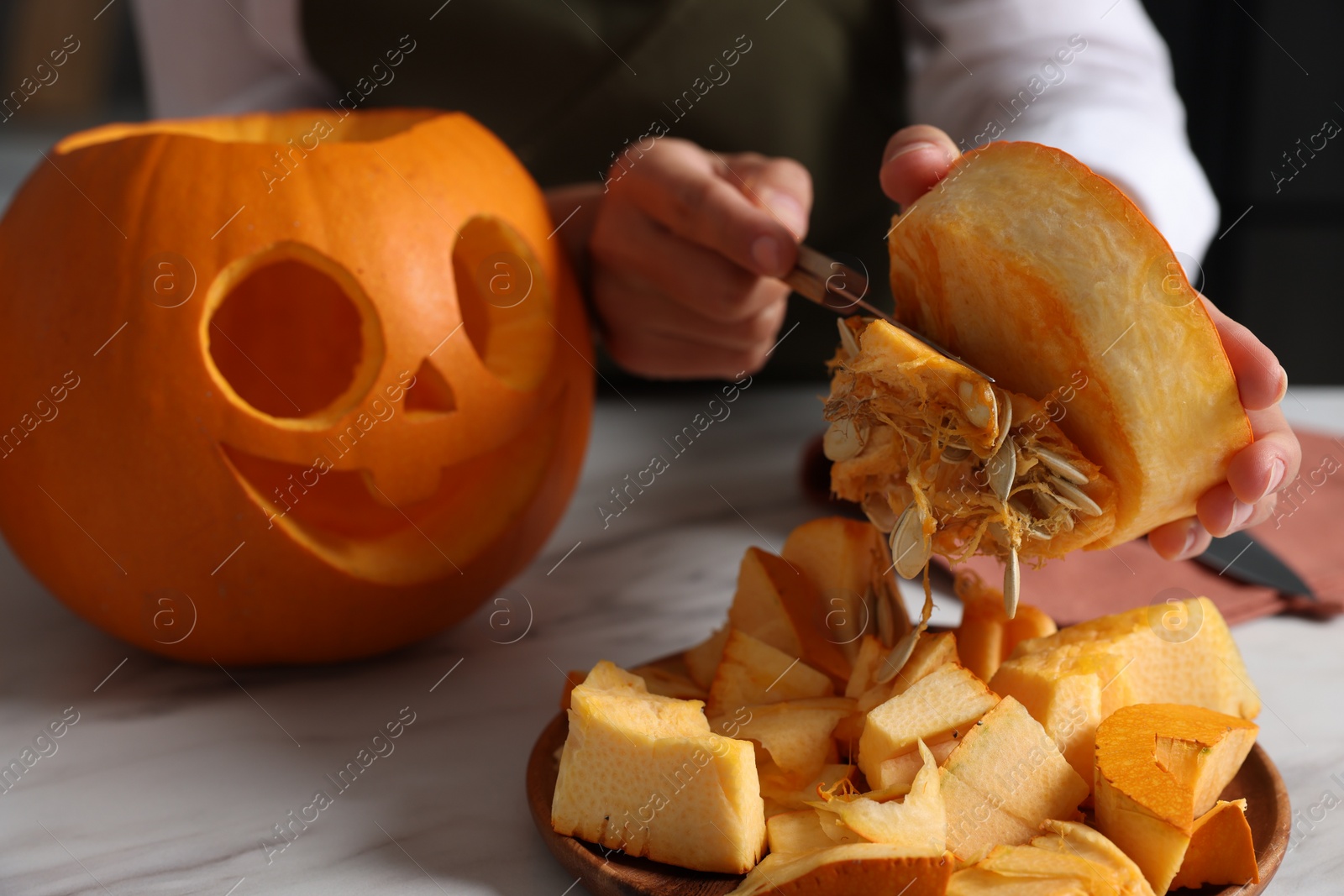 Photo of Woman carving pumpkin for Halloween at white marble table, closeup