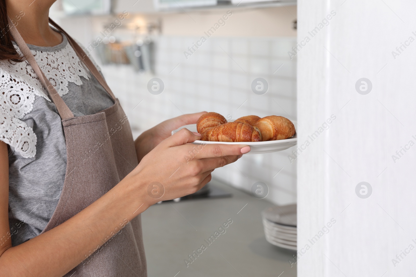 Photo of Young woman with plate of oven baked croissants in kitchen, closeup