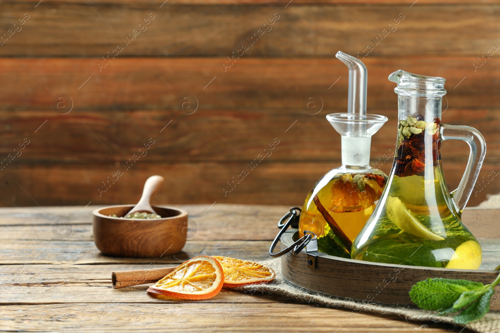 Photo of Cooking oil with different spices and herbs in jugs on wooden table. Space for text