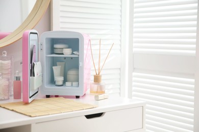 Photo of Cosmetics refrigerator and skin care products on white vanity table indoors