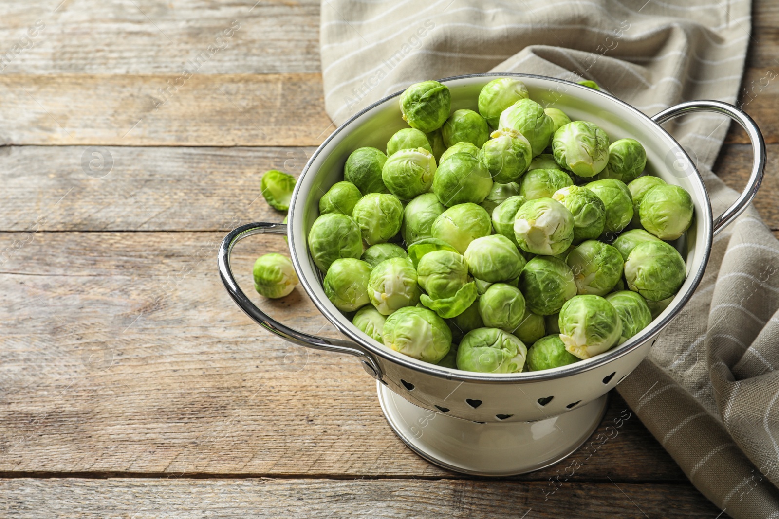 Photo of Colander with Brussels sprouts and cloth on wooden background. Space for text