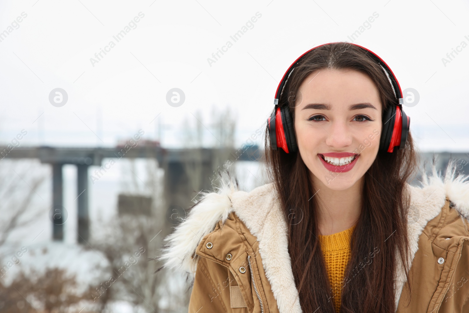 Photo of Beautiful young woman listening to music with headphones outdoors. Space for text