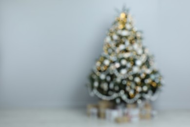 Photo of Blurred view of beautiful Christmas tree and gift boxes near light grey wall in room, space for text