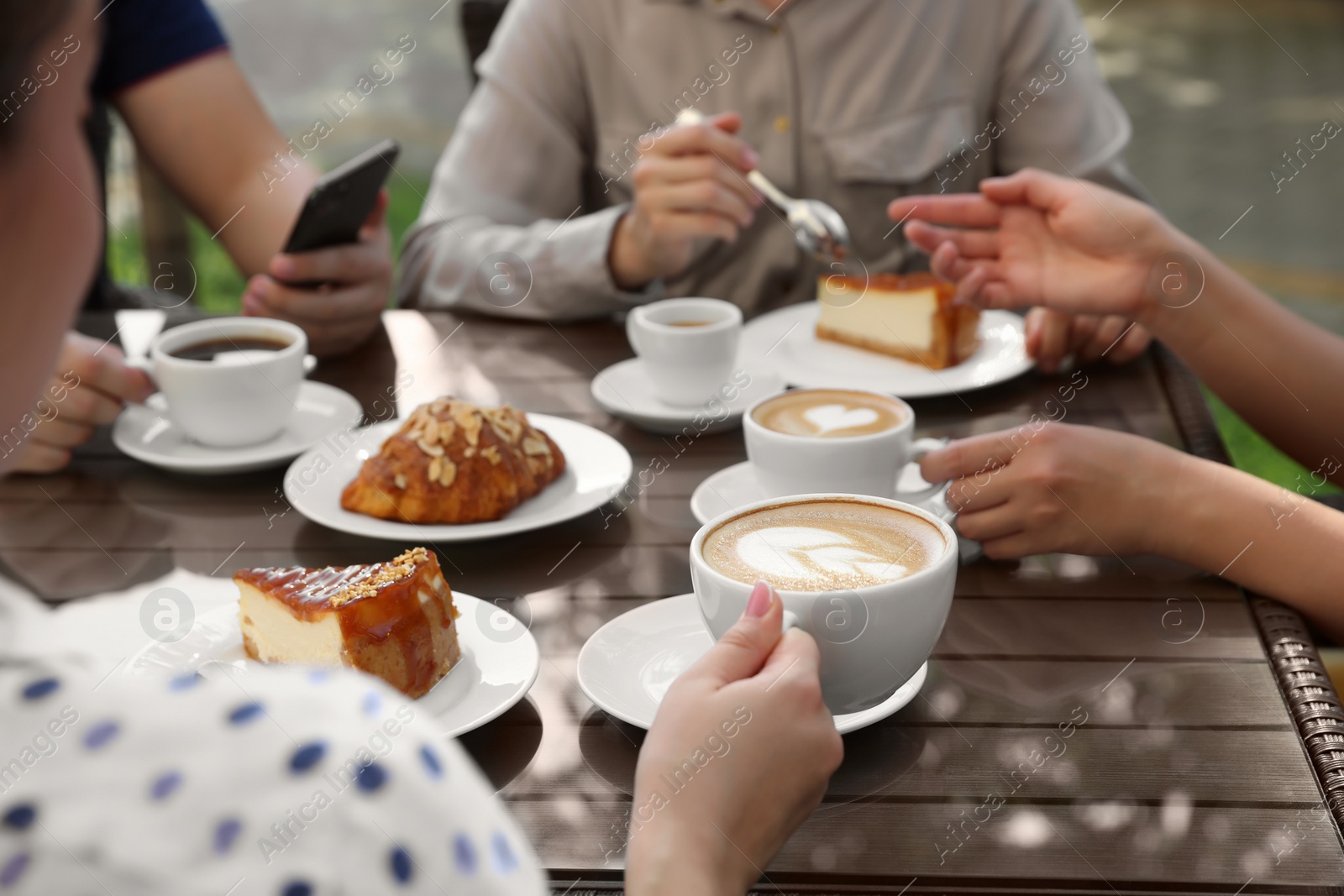 Photo of Friends drinking coffee at wooden table in outdoor cafe, closeup